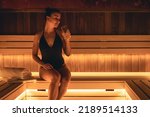 Attractive young woman in a swimsuit with a glass of water in the sauna.