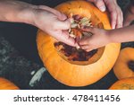 A close up of daughter and father hand who pulls seeds and fibrous material from a pumpkin before carving for Halloween. Prepares jack-o-lantern. Decoration for party. Little helper. Top view.