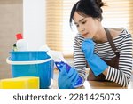 Closeup on woman in brown apron and blue rubber gloves with spray bottle of cleaning supplies reading instruction at home in kitchen. toxic cleaning supplies concept.
