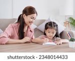 Small photo of Educational pastime develop creativity skill in kid concept. Asian mother her small daughter in sunny cozy living room, mom teach girl paint use paper and colourful pencils