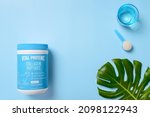 Small photo of KIEV, UKRAINE-NOVEMBER 10, 2021: Collagen Peptides Powder Jar with a measuring spoon and a glass of water on a blue background, top view. Collagen from the skins of grass-fed pasture cows, unflavored