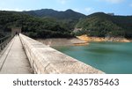 Small photo of Walkway on top of Tai Tam Upper Reservoir Dam (Hong Kong waterworks heritage built in 1888) on the left, with back of a couple at the further end, water and hills on the right side.