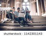 Students are spending time together.Multiethnic group of young people looking at a laptop and and sitting on steps in university hal