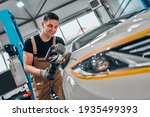 Auto mechanic worker polishing car at automobile repair and renew service station shop by power buffer machine. Selective focus. Close up view.