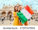 young man and woman holding italian flag in front of saint marks basilica at Venice, Italy