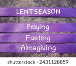 Small photo of Christianity concept about Ash Wednesday, Good Friday, Lent Season and Holy Week. LENT SEASON, PRAYING, FASTING and ALMSGIVING written on purple ribbons. With blurred background.