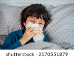 Small photo of Little child boy blowing his nose. Sick child with napkin in bed. Allergic kid, flu season. Kid with cold rhinitis, get cold snot nose