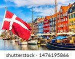 Copenhagen iconic view. Famous old Nyhavn port in the center of Copenhagen, Denmark during summer sunny day with Denmark flag on the foreground.