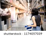 An asian woman doing shopping  and walking with her cart in cargo or warehouse. Boxes on rows of shelves in warm light background. copy space