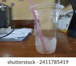 Small photo of Indonesia, January 12 2024: A plastic cup filled with leftover ice water. there lay a limp pink straw. located between the plug, tripod, calendar and printer.