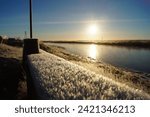Autumn, morning frost on a bench against the background of the river and the rising sun