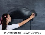 Small photo of A standing teenager wipes a dirty school blackboard with a wet sponge. The school blackboard is hanging on a white brick wall. A helpful girl stands at the blackboard.
