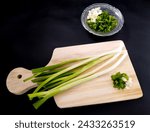 Small photo of Fresh green onions or spring onions on wooden board, isolated on black background. concept of cutting spring onions on a wooden cutting board