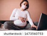 Pregnant woman wearing mask working from home on computer