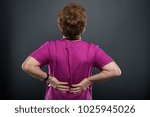 Small photo of Back view of senior lady doctor holding back like hurting on black background with copyspace advertising area