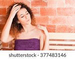 Attractive woman in purple towel warming in salt sauna and holding eyes closed