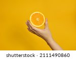 Small photo of The girl's hand holds a cut round slice of fresh tropical orange. An orange in a woman's hand on a yellow background is isolated. Orange slice. The girl gently holds a citrus in one hand