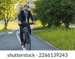 Small photo of Handsome young executive in elegant suit riding on bike lane in sunny day. Front view of busy businessman wearing protective helmet getting to work by bicycle on bike lane. Concept of bike commute.