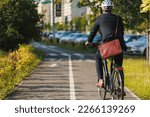 Small photo of Elegant entrepreneur in smart casual cycling on bicycle track in warm sunny day. Back view of tall male manager with brown leather laptop bag riding bike in sleeping area of city. Concept of activity.