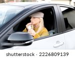 Elegant middle-aged woman eating chewing gum in a car behind the wheel