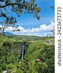 Small photo of Karo Waterfall's enchantment: Cascading waters amidst lush green hills, framed by a canvas of blue sky and clouds, creating a picturesque and serene scene