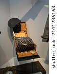 Small photo of Caen, France - June 20 2019 : Enigma Cipher Coding Machine from World War II, with hat on top at Caen Memorial Museum in Normandy.