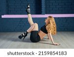 A young beautiful woman is sitting on a splits in a dance hall in high-heeled shoes