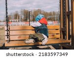 Small photo of The offended boy is sitting on a lifestyle bench . Childish grievances. Childish anger. An article about children's emotions. An article about the psychology of children. Transitional age