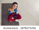 Small photo of Top view of a woman sitting on a sports mat with dumbbells in her hands and looking at the camera. Concept of physical training, home workout, sports articles and advertising. Banner. Place for text.