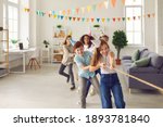 Small photo of Team of happy smiling diverse children in funny cone hats playing tug-of-war in spacious decorated room at birthday party at home. Group of kids enjoying exciting games in after school club or center