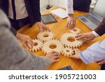 Cropped shot of team of company workers joining cogwheels on office table as metaphor for collaboration, teamwork, good business system, finding working solutions and effective management