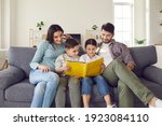 Small photo of Happy young family with children enjoying free time resting on couch at home. Parents and kids sitting on soft comfy sofa, reading book of fairy tales or looking through holiday photo album together