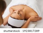 Small photo of Cosmetologist or masseur making manual relaxing rejuvenating massage for face and shoulders for young woman in beauty salon, rear view. Rejuvenating facial massage in cosmetology