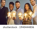 Happy creative team holding glowing lit lightbulbs. Diverse collaboration group of intelligent young multicultural business people with shining light bulbs presenting and sharing effective useful idea
