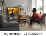 Happy lady enjoying funny TV show sitting in comfy armchair at home. Young woman relaxing in comfortable chair in living-room and watching music video on television