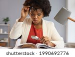 Surprised inquisitive black woman with magnifying glass takes off glasses as she sees an amazing curious fact in the book she's reading. Shocked financial advisor studying business documents in office