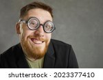 Small photo of Funny curious man wearing retro vintage thick rimmed glasses smiling at camera. Studio closeup of excited eccentric crazy nerd with ginger beard in suit and uncool old-fashioned round frame spectacles