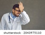 Small photo of Damn idiot. Emotional male doctor smacks forehead as he remembers stupid mistake, foolish medical fiasco or professional failure at hospital, feeling dumb, annoyed and awkward, copy space background
