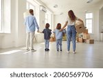 Small photo of Family standing in empty unfurnished spacious living room, rear view, from behind. Mom, dad and kids carrying and unpacking boxes together while moving into house or apartment. Buying new home concept