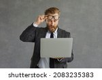 Oh my god, incredible. Excited surprised shocked man takes off glasses looking at laptop computer screen isolated on grey background. Lucky businessman makes deal or gets business email with good news
