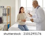 Small photo of Experienced senior doctor at modern clinic talking to nervous female patient. Supportive adult physician trying to calm down worried young woman and asking her to relax before medical exam