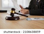 Small photo of Law, auctioning, corruption, bankruptcy, bail, bribery or fines. Close up of judge gavel standing on sound block and bundle of dollars on table against background of judge or auctioneer with documents
