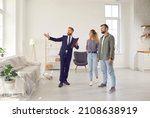 Small photo of Realtor or real estate agent giving potential buyers or tenants tour about big house. Boyfriend and girlfriend or husband and wife who consider buying property looking at new modern spacious home