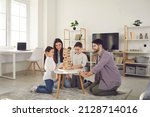 Happy family with kids playing board games at home. Smiling mom, dad and children sitting on the floor around a low table in a cozy living room and pulling wooden blocks from the tower