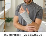 Small photo of Crop unwell man with bandage on broken hand have rehabilitation at home. Guy struggle with arm injury or trauma wear protective splint on wrist after accident. Rehab and treatment. Healthcare.