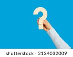 Small photo of Wooden question mark in human hand on empty blue background. FAQ, asking question, being unsure, seeking truth, guessing, unclear answer, mystery, secret, riddle, confusion, exam, consultation concept