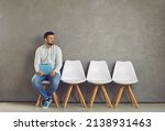 Small photo of Worried young caucasian male job seeker vacancy candidate holding resume form waiting for interview meeting sitting on chair looking aside. Jobless applicant at recruitment staffing agency