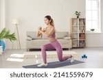 Small photo of Happy fit woman having indoor fitness workout. Active slim young Caucasian girl in modern light mauve or pale purple pink color sportswear doing forward lunges exercise standing on gym mat at home