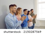Small photo of Group of happy joyful young people applaud at business conference or team meeting. Side view of smiling modern business men and women standing in row near wall and applauding their leader.