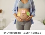 Small photo of Mother thinking of name for future baby. Woman trying to guess gender of unborn child. Pregnant lady with question mark sticky notes on big bare belly, cropped shot. Name choice, gender reveal concept